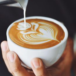 Latte art being poured into a cup, creating a floral design on the coffee surface.