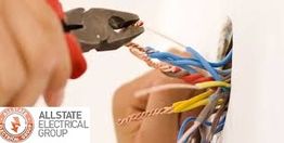 Person using pliers to twist electrical wires beside a wall outlet.