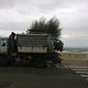 Camion per la raccolta rifiuti parcheggiato vicino alla spiaggia, cielo nuvoloso sullo sfondo.