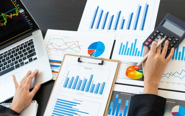 Eine Frau sitz vor Dokumenten auf denen Diagramme, Daten und Zahlen abgebildet sind, um einen Businessplan für eine digitale Strategie zu entwickeln.