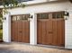 Two wooden garage doors with windows and wall-mounted lanterns on a white building.