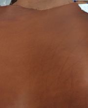 Pieza grande de cuero marrón extendida sobre una mesa junto a papeles blancos.