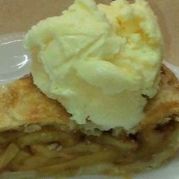 Slice of apple pie topped with a scoop of vanilla ice cream on a plate.