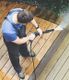 Man using a pressure washer on a wooden deck.