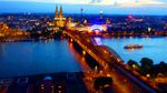 Blick bei Nacht auf eine beleuchtete Stadt mit einem Fluss und einer großen Kathedrale im Hintergrund.