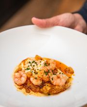 Un plato de camarones en salsa anaranjada con hierbas, sostenido por una mano.