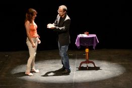 Un mago realiza un truco para una espectadora en un escenario iluminado.