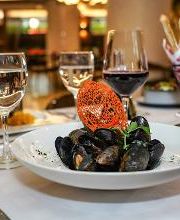 Plato de mejillones en mesa elegante con copas de vino y pan al fondo.