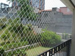 Rede de proteção em sacada com jardim e prédios ao fundo.