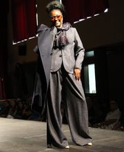 Frau auf Modenschau trägt Anzug mit Mantel, Sonnenbrille und modischem Schal.