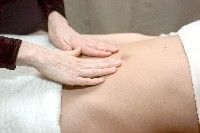 Hände massieren einen Bauch auf einer Liege.