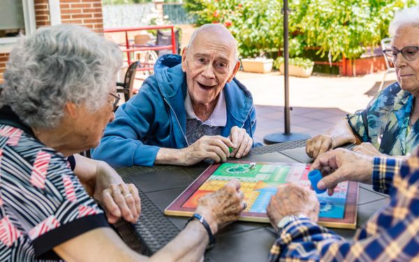 Seniorinnen und Senioren sitzen gemeinsam an einem Tisch und spielen ein Brettspiel im Freien.