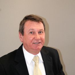 Eine Person im Anzug lächelt freundlich in die Kamera vor einem neutralen, grauen Hintergrund.