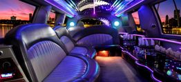 Luxurious limousine interior with neon lights and cityscape at sunset in the background.