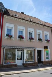 Zweistöckiges rosa Haus mit vier Fenstern und Blumen im Erdgeschoss, markise über Schaufenster.