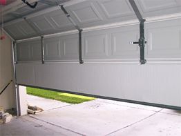 Half-open garage door, view from inside, showing driveway and grassy area outside.