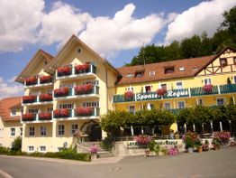 Gelbes Gebäude mit blühenden roten Blumen, blauer Himmel und Bäume im Hintergrund.