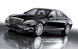 Auto di lusso nera su sfondo bianco, riflessa sul pavimento lucido.