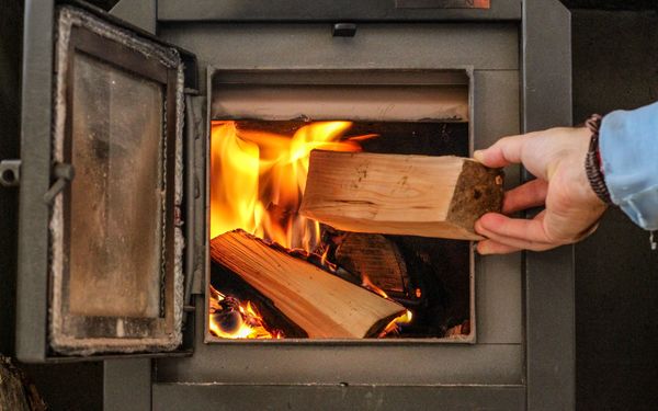 Eine Person legt einen Holzscheit in einen Holzofen.