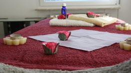 Massagetisch mit roten Rosen, Handtüchern, Kerzen und einer blauen Flasche in entspannter Atmosphäre.