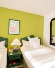 Habitación con dos camas, una pared verde, espejo grande y lámpara entre las camas.