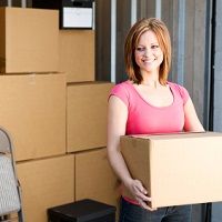 Woman smiling while holding a cardboard box in a storage unit.