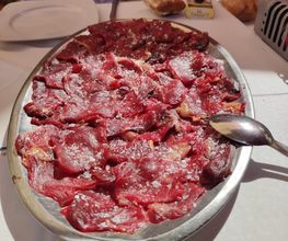 Plato de carne cruda en rodajas sobre una mesa, con personas alrededor.