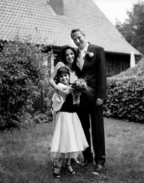 Eine lächelnde Familie im Garten posiert für ein Schwarz-Weiß-Foto vor einem Haus mit Satteldach.