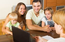 Family at a table listening to a person behind a laptop, discussing something with interest.