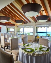 Restaurante elegante con vista al mar, mesas preparadas y techo de vigas de madera.