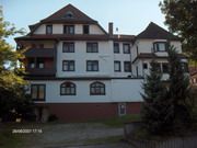 Ein großes, mehrstöckiges Haus mit weißen Wänden und dunklem Dach, umgeben von Bäumen.