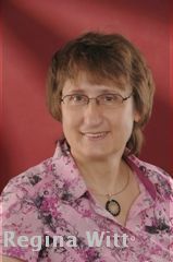 Eine Frau mit Brille lächelt vor rotem Hintergrund. Sie trägt ein pink gemustertes Hemd.