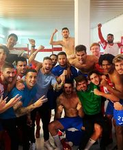 Grupo de personas celebrando en un vestuario. Algunos visten ropa deportiva.