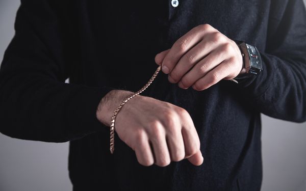 Mann mit Uhr zieht sich Goldarmband an