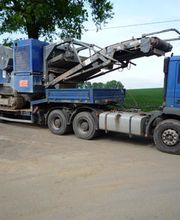 LKW mit Aufleger transportiert große Baumaschine auf einer Landstraße.