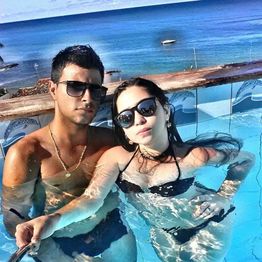 Casal de óculos de sol posando em piscina com vista para o mar ao fundo.