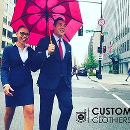 Two people in business attire walking under a pink umbrella in an urban setting.