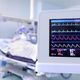 Close-up of a heart monitor displaying vital signs in a hospital room with a patient in the background.