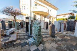 Steinausstellung im Freien vor einem weißen Gebäude mit mehreren Grabsteinen auf gepflastertem Boden.