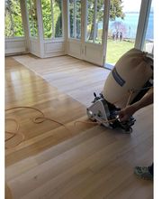 Holzboden wird in hellem Zimmer mit Seeblick geschliffen. Schleifmaschine im Einsatz.