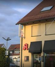 Gebäude mit Apotheke auf der Ecke, umgeben von Häusern, bei teilweise bewölktem Himmel.