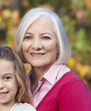 Drei Generationen von Frauen lächeln im Freien vor herbstlichem Hintergrund.