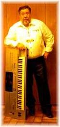 Mann in weißem Hemd steht mit einem Keyboard vor einer Holzwand.