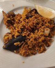 Plato de paella de mariscos con trozo de limón en un plato cuadrado blanco.