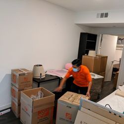Person packing boxes in a room with stacked boxes and a kettle on a table.