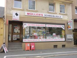 Fassade eines Schreibwarenladens mit Schaufenster und Werbeschildern, "Müller's Schreibblädla".