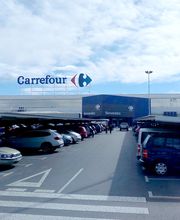 Aparcamiento con coches frente a supermercado Carrefour bajo un cielo parcialmente nublado.