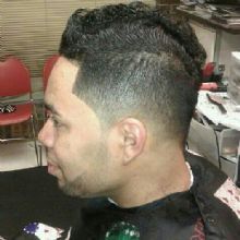 Man with a styled haircut featuring a fade and curls, sitting in a barbershop chair.