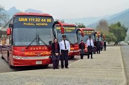 Red tour buses lined up with staff standing in uniform in front, mountains in the background.