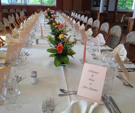 Langer, weiß gedeckter Tisch mit Blumenarrangement und eleganten Gedecken in einem Festsaal.